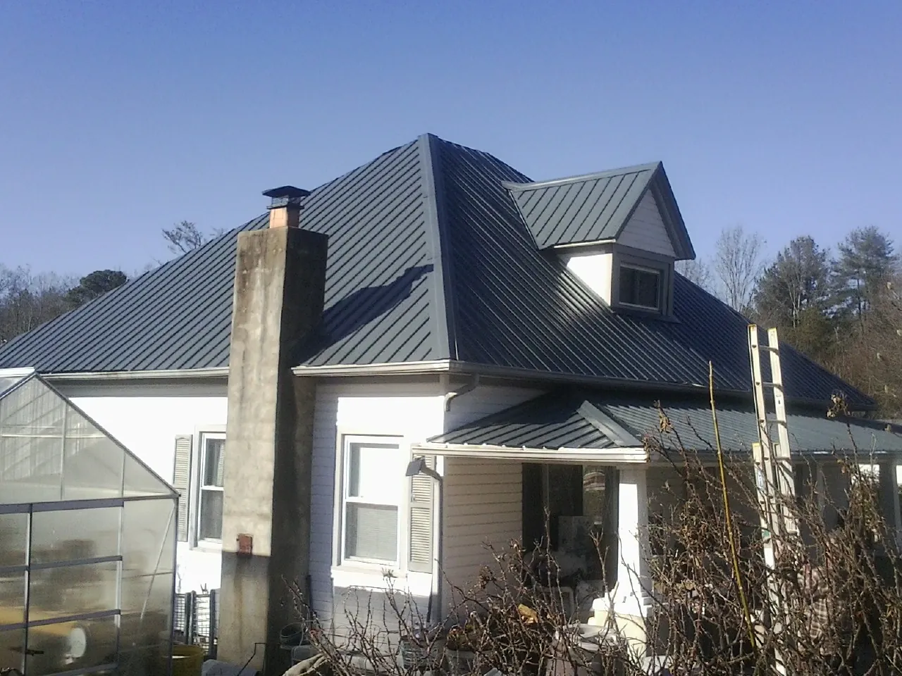 Dark blue standing seam metal roof on a white farmhouse with dormer — Slate & Tile Roof Repair by Roofing Brothers in Saint Johnsville
