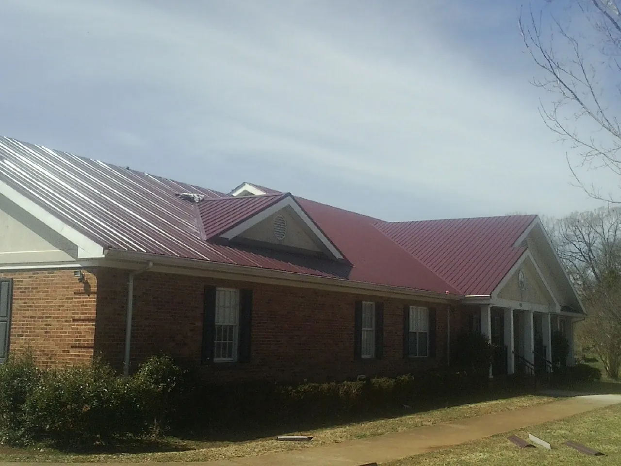 Red metal roof with gabled entries on a long brick building, from a Hail Damage Roof Repair job in Saint Johnsville