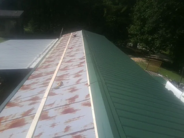 Old rusted panels beside newly installed green metal roofing — Wind Damage Roof Repair by Roofing Brothers in Saint Johnsville