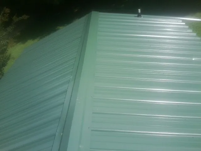 New green metal panels meeting at the ridge of a roof — Flat Roof Repair work by our crew in Saint Johnsville
