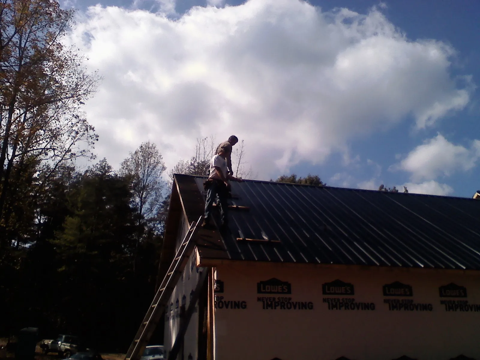 Roofer fastening dark metal panels high against a cloudy sky, from a Roof Inspection job in Saint Johnsville