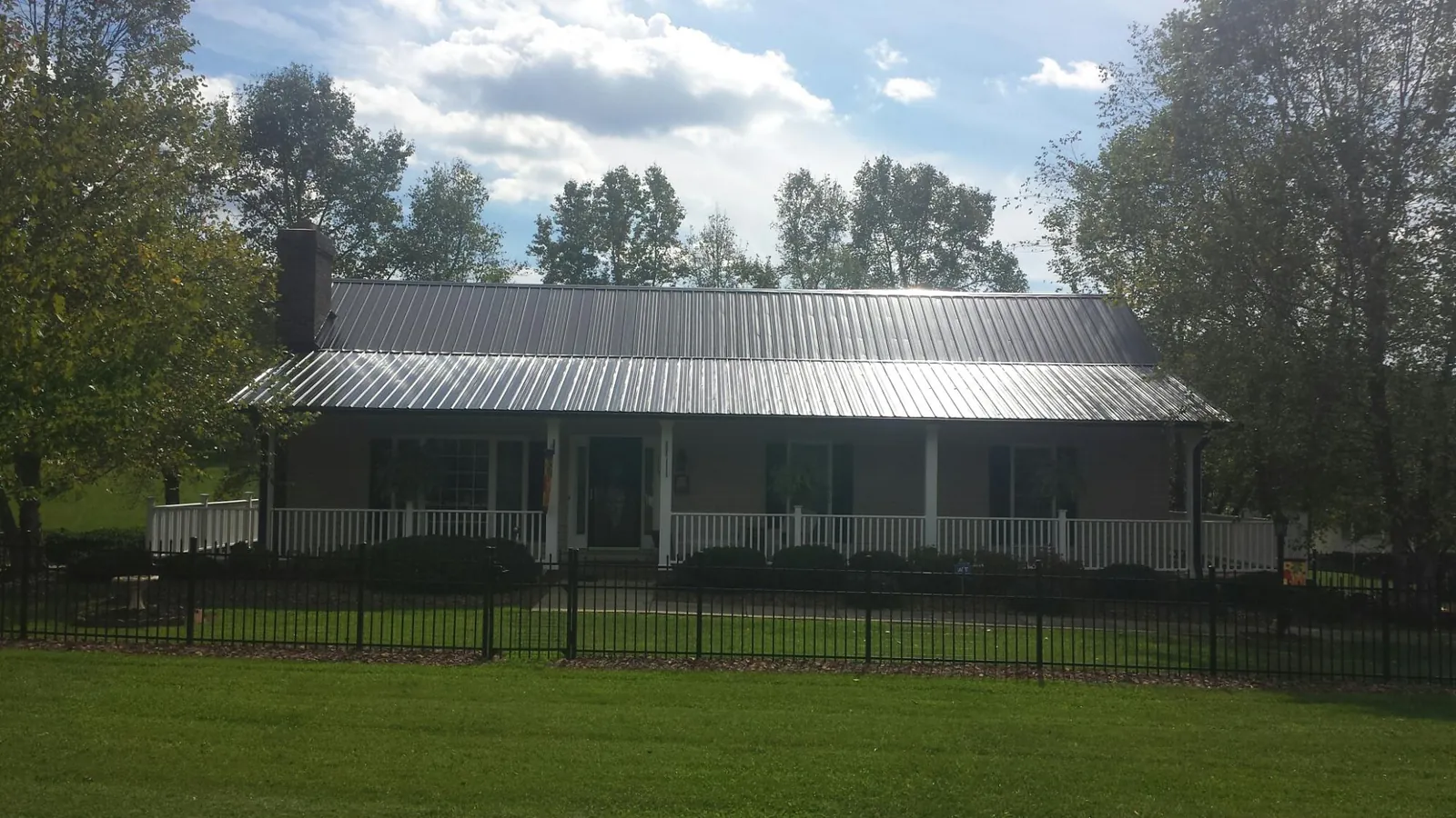 Gray metal roof on a brick ranch with a full width front porch — Gutter Guard Installation work by our crew in Saint Johnsville