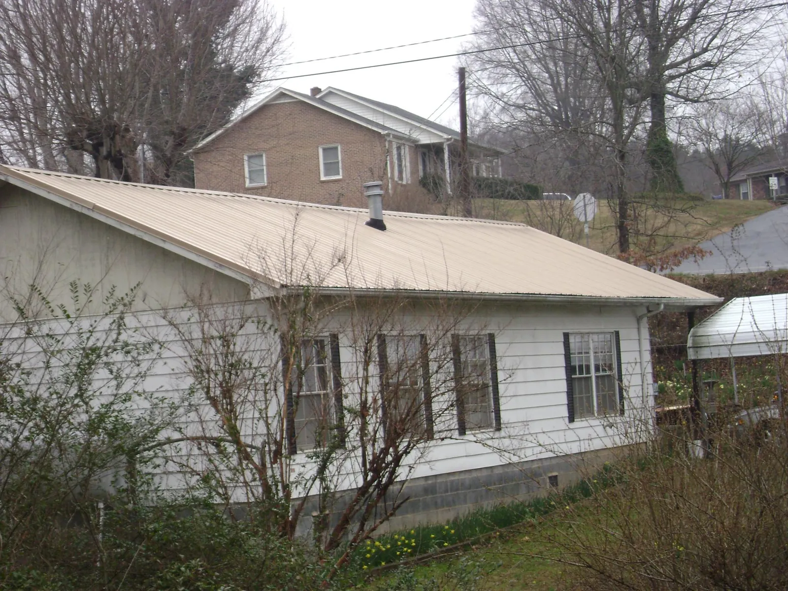Tan metal roof on a white sided house set into a hillside — Commercial Roofing by Roofing Brothers in Saint Johnsville