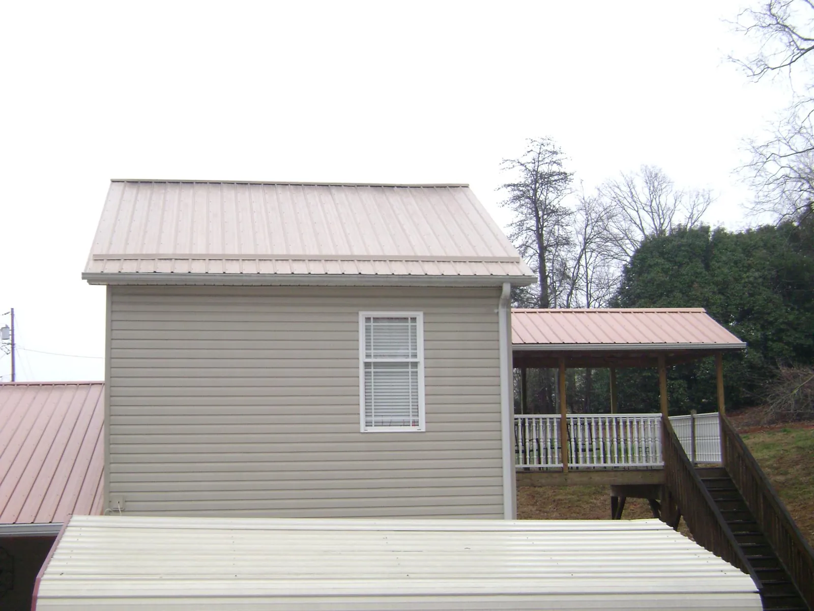 Tan metal roofs on a two story addition and attached porch, from a Roof Replacement job in Saint Johnsville